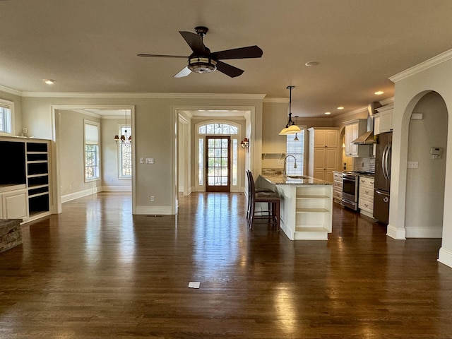 kitchen featuring wall chimney range hood, dark wood finished floors, a kitchen breakfast bar, stainless steel appliances, and a sink