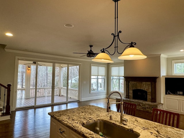 kitchen featuring open floor plan, a stone fireplace, crown molding, and a sink