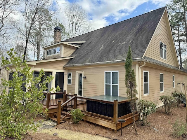 back of house with a shingled roof, a wooden deck, and a chimney