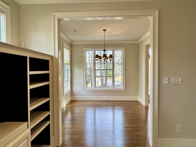 unfurnished dining area featuring an inviting chandelier, baseboards, dark wood-style flooring, and ornamental molding