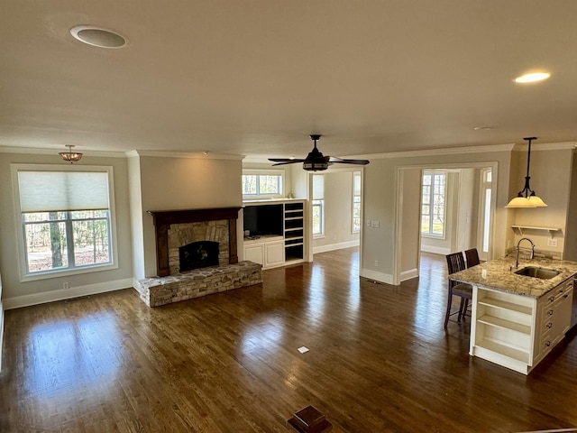 unfurnished living room featuring dark wood-type flooring, ornamental molding, a fireplace, and a sink