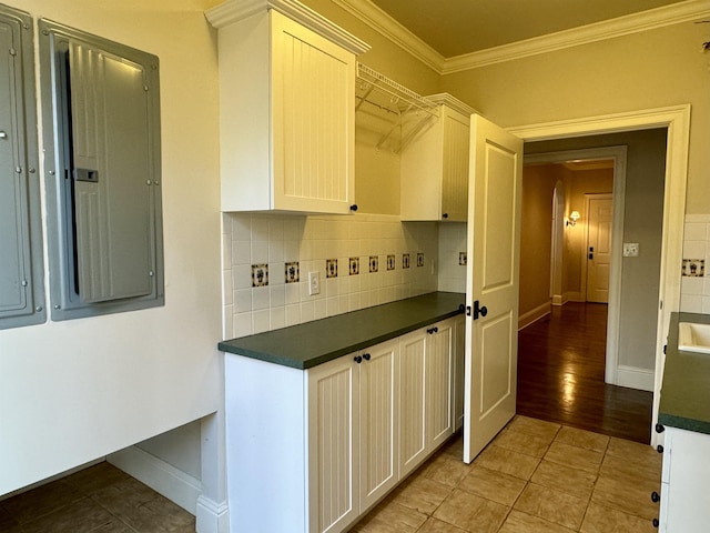 kitchen with dark countertops, backsplash, ornamental molding, electric panel, and arched walkways