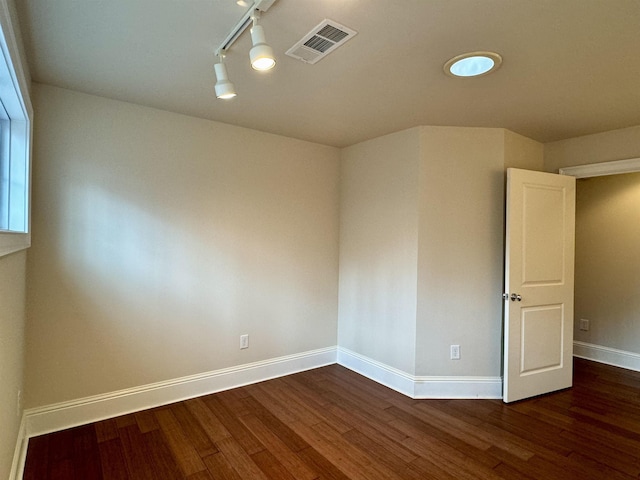 unfurnished room with track lighting, wood finished floors, visible vents, and baseboards