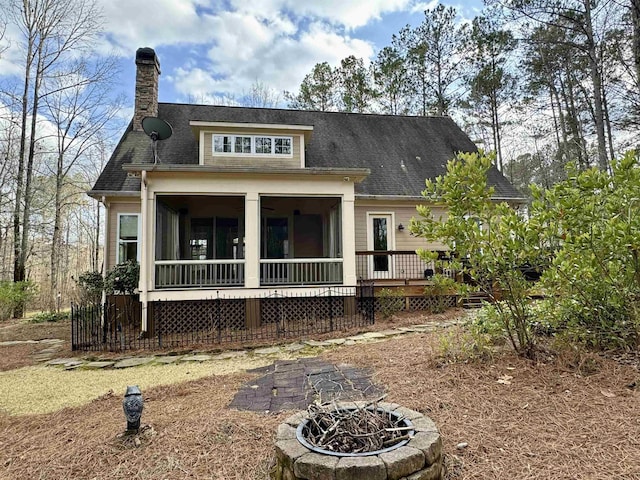 rear view of property with a fire pit, roof with shingles, a sunroom, a wooden deck, and a chimney