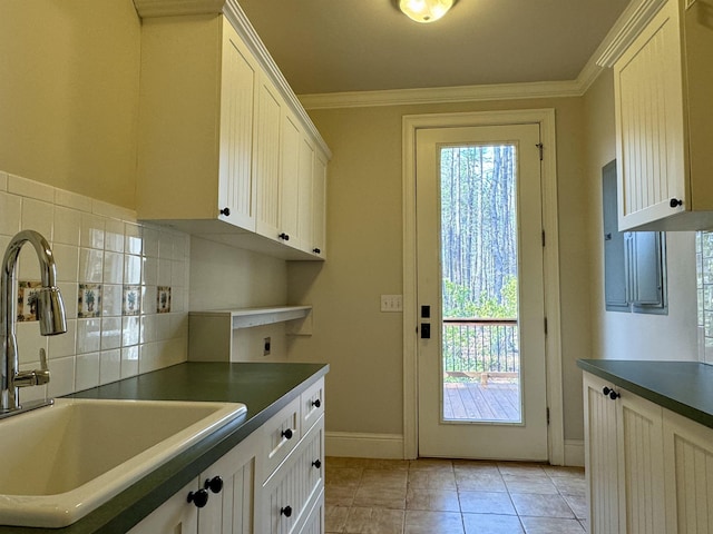 kitchen with dark countertops, ornamental molding, light tile patterned floors, white cabinetry, and a sink