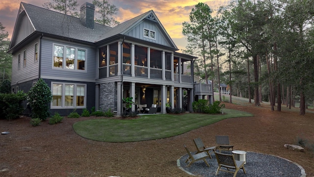 back house at dusk with an outdoor fire pit, a sunroom, and a lawn