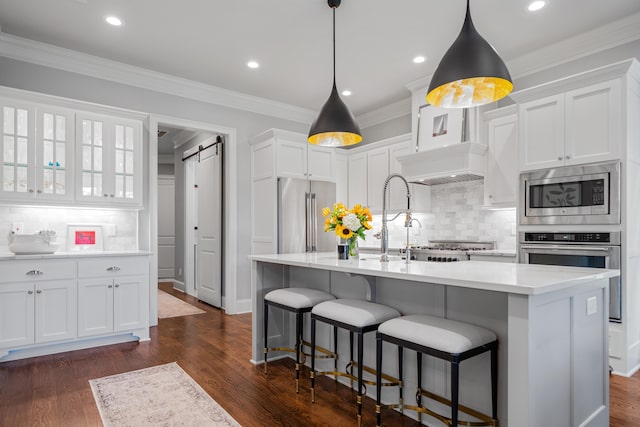 kitchen featuring stainless steel appliances, a barn door, a center island with sink, and white cabinets