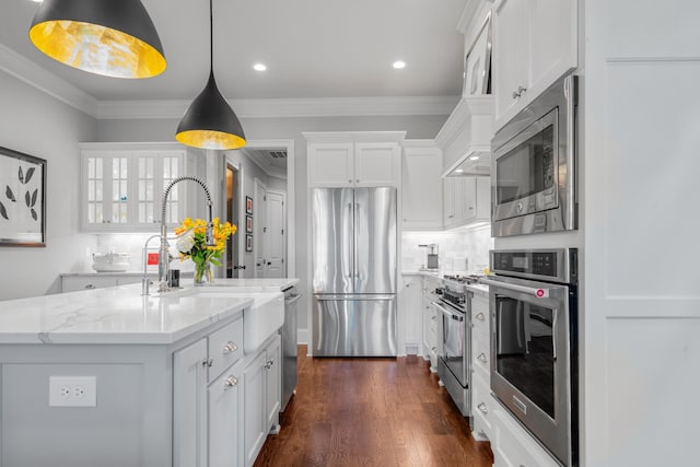 kitchen featuring a kitchen island with sink, white cabinetry, stainless steel appliances, light stone countertops, and decorative light fixtures