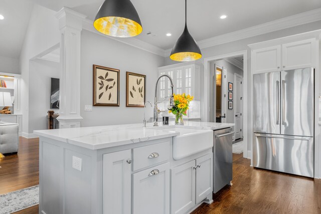 kitchen featuring white cabinetry, hanging light fixtures, a center island with sink, stainless steel appliances, and decorative columns