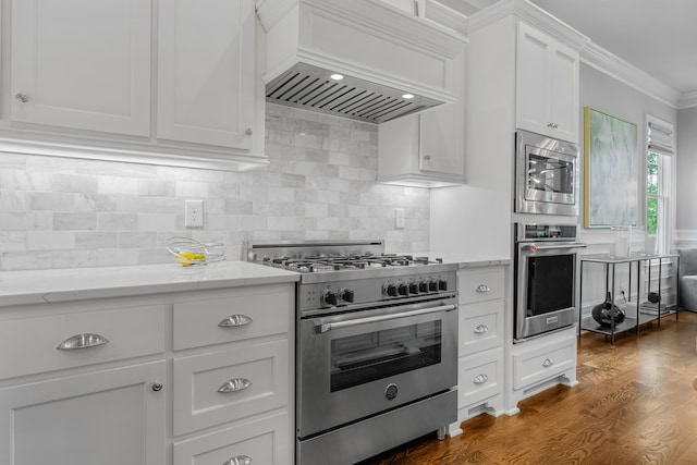 kitchen with stainless steel appliances, light stone countertops, ornamental molding, white cabinets, and custom exhaust hood