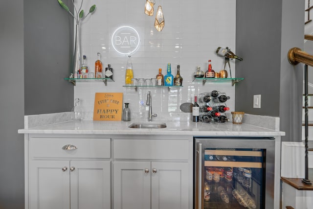 bar featuring light stone counters, beverage cooler, sink, and white cabinets