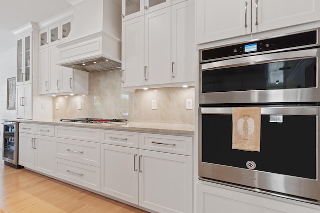 kitchen with custom exhaust hood, wine cooler, stainless steel appliances, backsplash, and white cabinets
