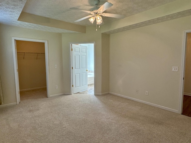 unfurnished bedroom with a walk in closet, light carpet, a textured ceiling, and a closet