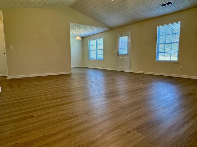 spare room featuring vaulted ceiling, hardwood / wood-style floors, and a textured ceiling