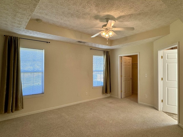 spare room featuring a raised ceiling, ceiling fan, light carpet, and a textured ceiling