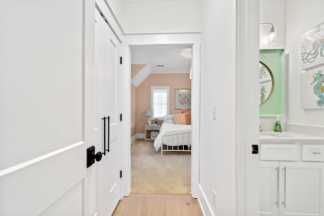 hall with visible vents, ornamental molding, light wood-style floors, and a sink