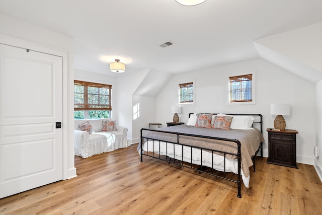 bedroom featuring visible vents, light wood-type flooring, baseboards, and vaulted ceiling