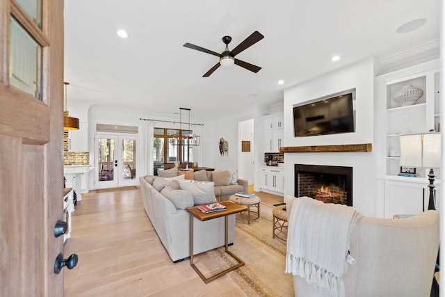 living room featuring light wood-style flooring, recessed lighting, a warm lit fireplace, french doors, and crown molding