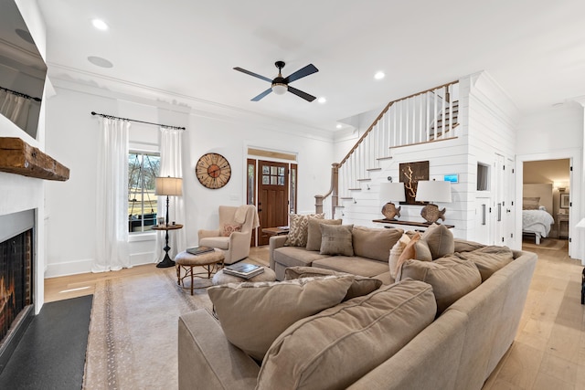 living area featuring stairway, a lit fireplace, wood finished floors, and crown molding