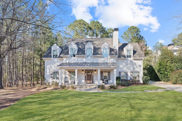 new england style home featuring a standing seam roof, a porch, a front yard, metal roof, and a chimney