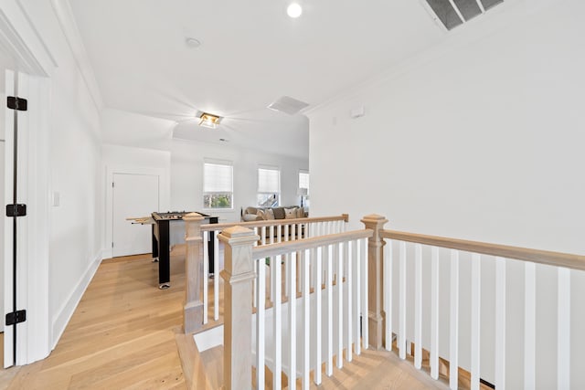 corridor with crown molding, light wood-style floors, visible vents, and baseboards