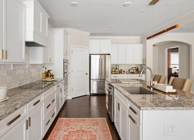 kitchen featuring high end fridge, a center island with sink, a sink, arched walkways, and black electric cooktop