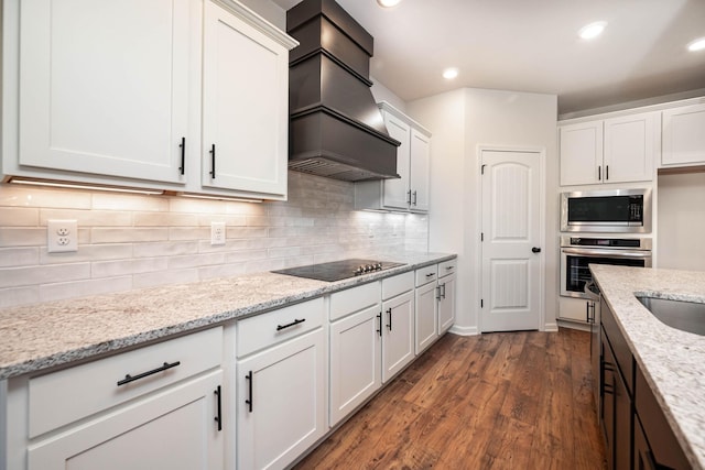 kitchen with premium range hood, white cabinetry, tasteful backsplash, light stone counters, and appliances with stainless steel finishes