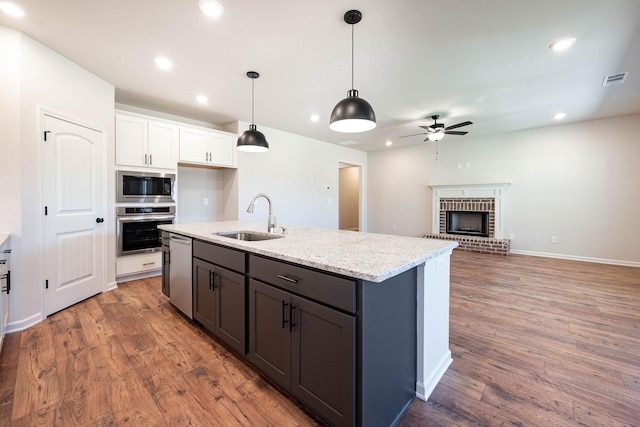 kitchen featuring appliances with stainless steel finishes, white cabinetry, sink, hanging light fixtures, and light stone counters