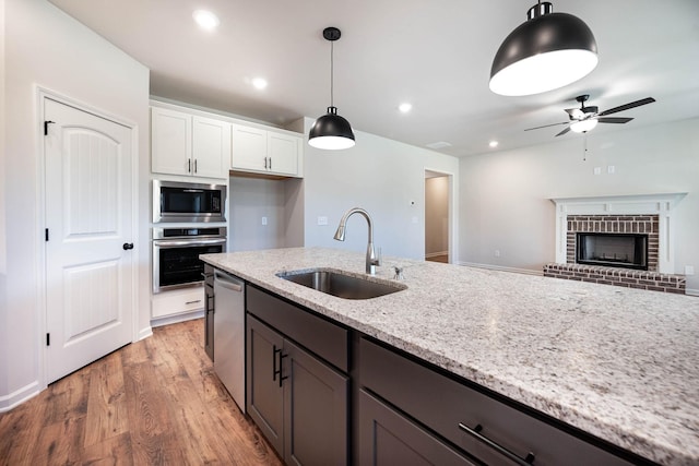 kitchen featuring appliances with stainless steel finishes, white cabinetry, sink, hanging light fixtures, and light stone countertops