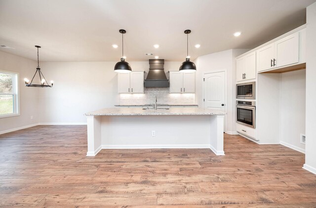 kitchen with light stone countertops, a center island with sink, stainless steel appliances, and premium range hood