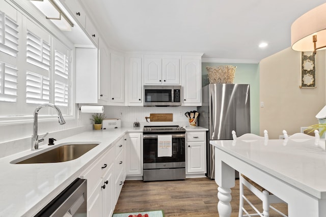 kitchen featuring appliances with stainless steel finishes, dark wood-type flooring, crown molding, white cabinetry, and a sink