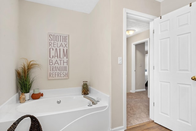 full bathroom featuring a textured ceiling, wood finished floors, a bath, and baseboards