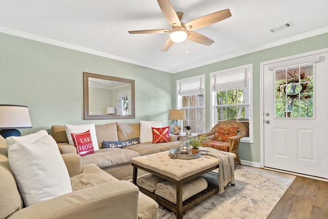 living room with crown molding, light wood finished floors, visible vents, a ceiling fan, and baseboards