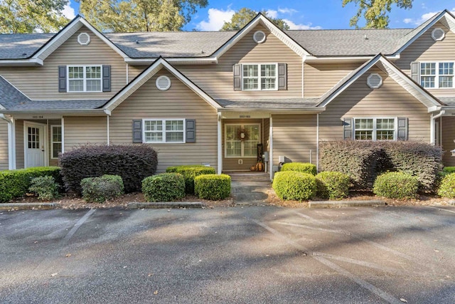 multi unit property featuring a shingled roof and uncovered parking