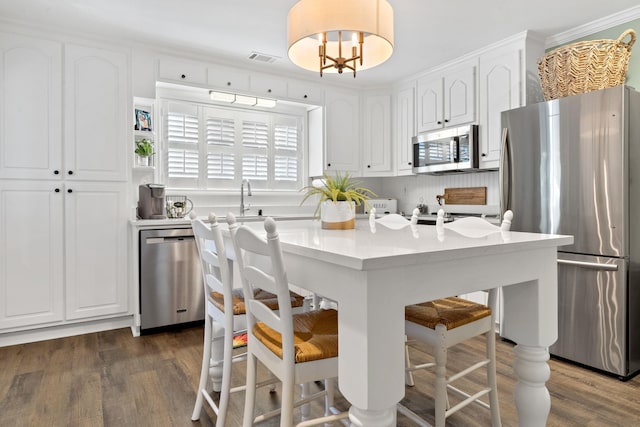 kitchen with appliances with stainless steel finishes, white cabinets, dark wood-type flooring, and a kitchen breakfast bar