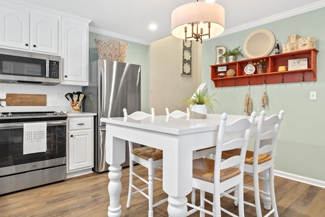 kitchen with appliances with stainless steel finishes, wood finished floors, white cabinetry, and crown molding