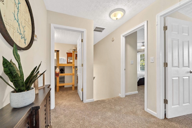 hall featuring light carpet, a textured ceiling, visible vents, and baseboards