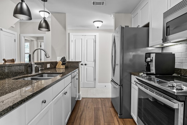 kitchen with appliances with stainless steel finishes, white cabinetry, sink, dark stone counters, and hanging light fixtures