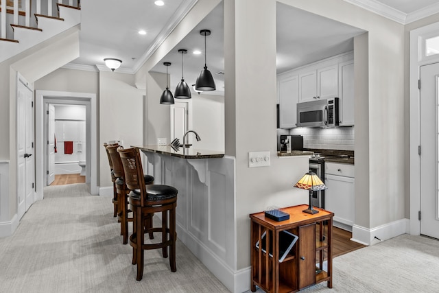 kitchen with dark stone countertops, ornamental molding, stainless steel appliances, and white cabinets