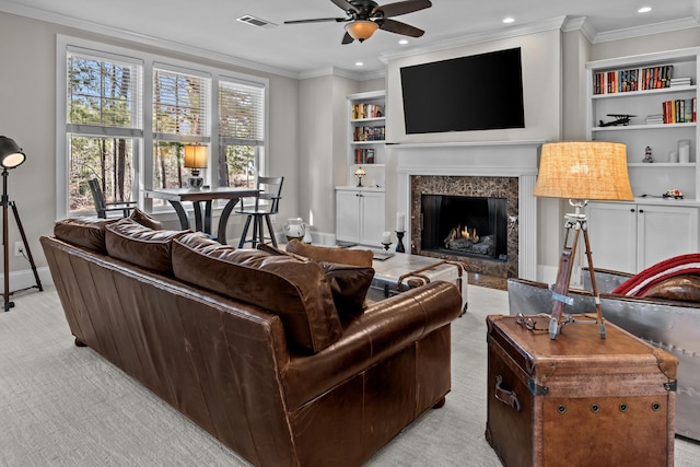 carpeted living room with built in shelves, ceiling fan, ornamental molding, and a premium fireplace