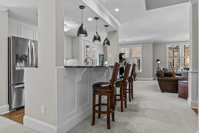 kitchen featuring decorative light fixtures, white cabinets, ornamental molding, light stone counters, and stainless steel fridge with ice dispenser