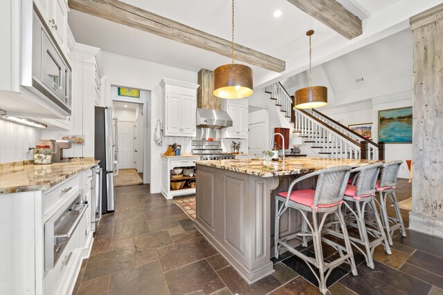 112 Arbors Ln, Eatonton, GA 31024 - kitchen with beam ceiling, stone tile floors, white cabinetry, stove, and range hood