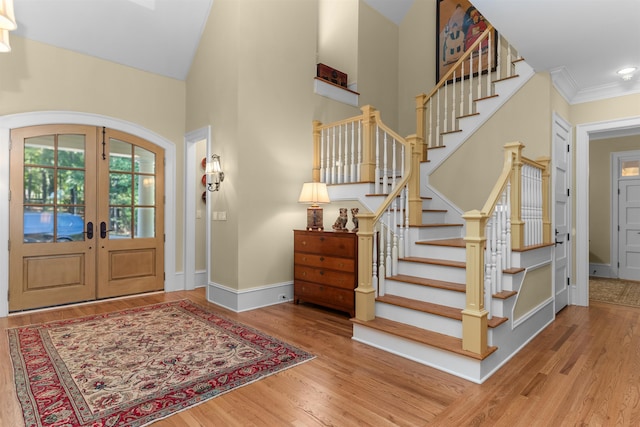 foyer featuring wood-type flooring, ornamental molding, high vaulted ceiling, and french doors