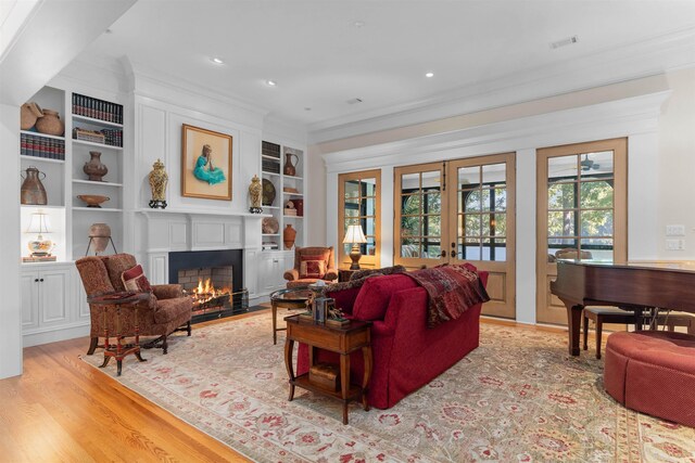 living room with french doors, built in features, crown molding, and light hardwood / wood-style flooring