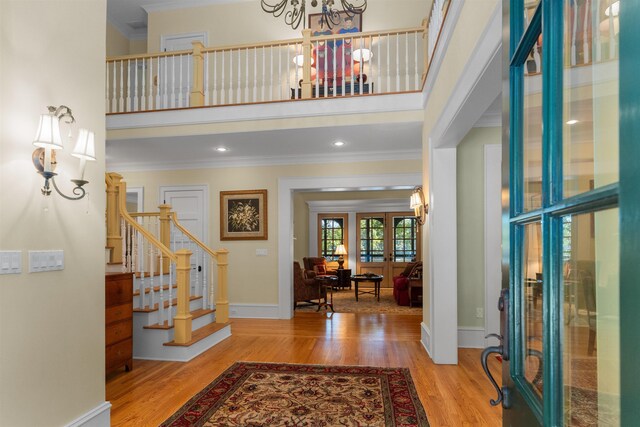 entrance foyer featuring hardwood / wood-style flooring, a high ceiling, a notable chandelier, ornamental molding, and french doors