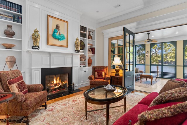 living area featuring built in shelves, ceiling fan, ornamental molding, and light wood-type flooring