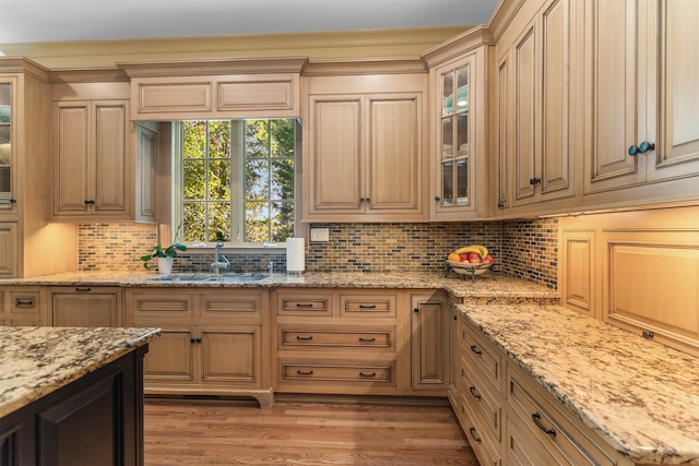 kitchen with sink, backsplash, hardwood / wood-style floors, light stone counters, and light brown cabinetry