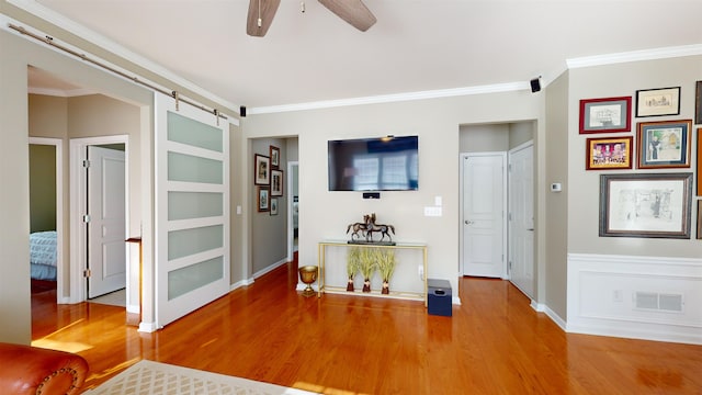 interior space with crown molding, wood-type flooring, a barn door, and ceiling fan