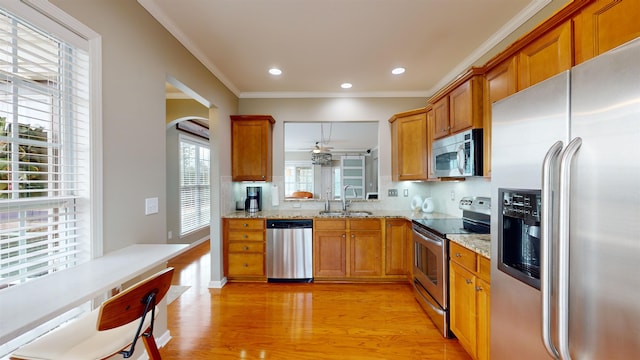 kitchen featuring sink, ornamental molding, light stone counters, light hardwood / wood-style floors, and stainless steel appliances