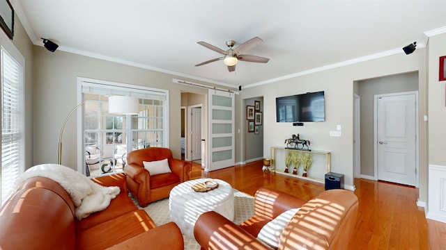 living room with crown molding, ceiling fan, a barn door, and light hardwood / wood-style floors